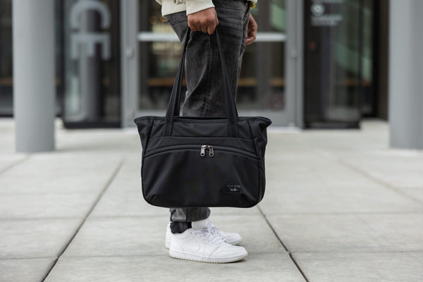 A person holding a Nomad Tote by the handles.